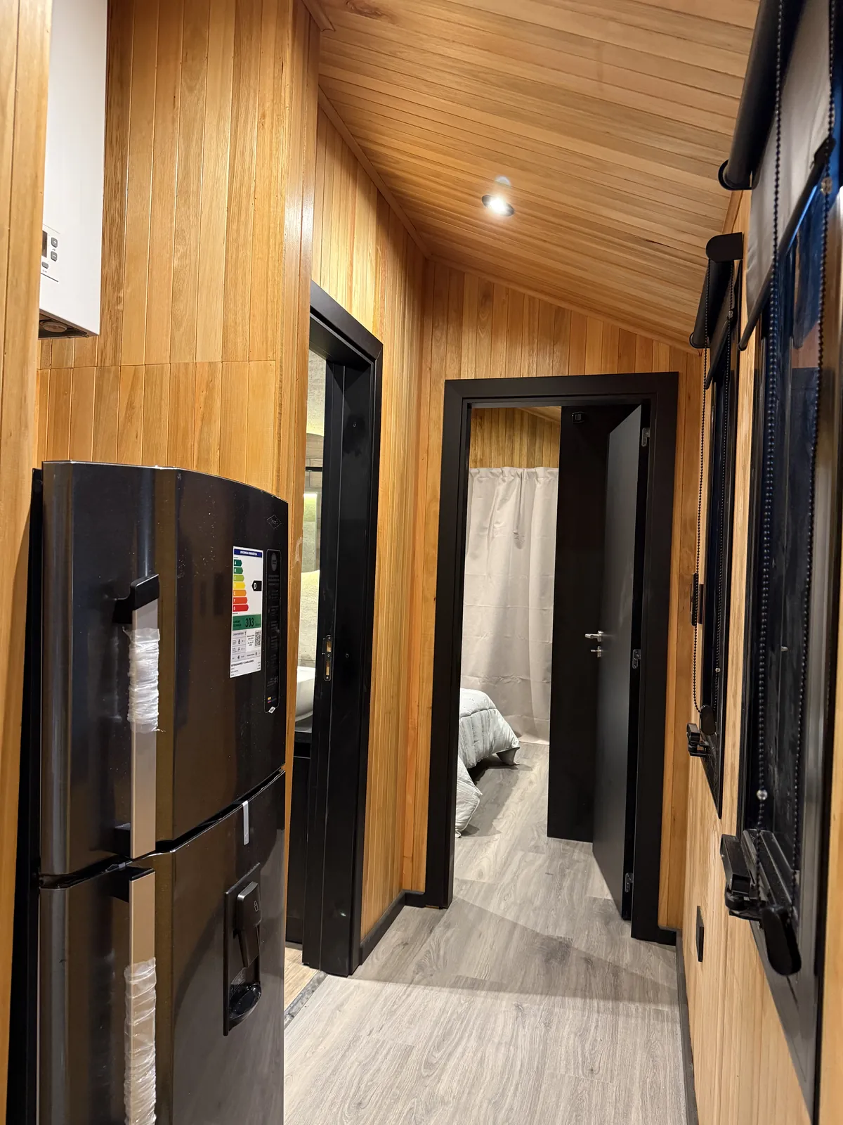 Pasillo revestido en madera con heladera integrada y vista al dormitorio casa modular Faci House